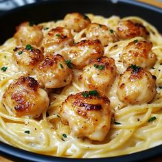 pasta with scallops and parmesan cheese in a black bowl on a wooden table