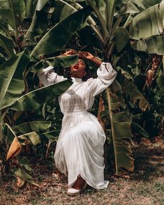 a woman in a white dress is sitting on the ground next to some banana trees