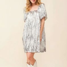 On an ivory background is a model wearing a silver sequin dress with a square neck and puff sleeves. Sequin Dress With Cowboy Boots, Sequin Dress With Boots, Sequin T Shirt Dress, Dresses With Cowboy Boots, Dazzling Dress, Babydoll Mini Dress, Dress Silver, Silver Dress, Boots Outfit