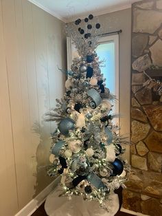 a white christmas tree with blue and silver ornaments on it in a living room next to a stone fireplace