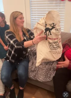 two women are sitting on a couch and one is holding a bag with reindeer designs