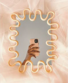 a hand holding a cell phone in front of a mirror with yellow spirals on it