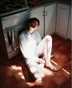 a man sitting on the floor in front of an oven with his legs spread out