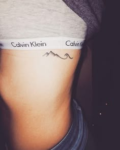 a woman's stomach with the word calm written on it and mountains behind her