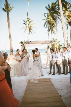 a couple getting married on the beach with their wedding party watching them walk down the aisle