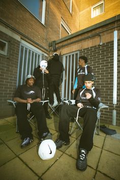 four people sitting in chairs with one person holding a soccer ball and the other standing behind them