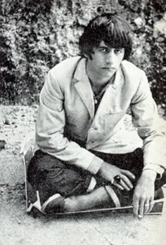 a young man sitting on the ground with his skateboard in front of him and looking at the camera