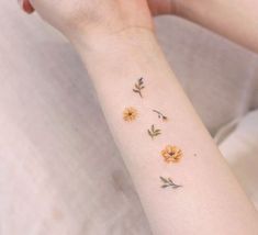 a woman's arm with yellow flowers on the left side of her wrist and two small daisies on the right hand