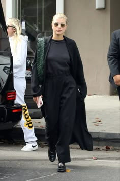 the blonde woman is walking down the street in her black jumpsuit and white sneakers