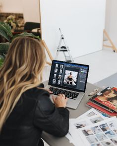 a woman sitting at a table with a laptop on her lap looking at the screen