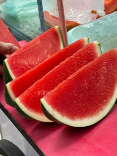 slices of watermelon sit on a pink table with other fruit in the background