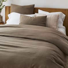 the bed is made with brown linens and white pillows, along with a potted plant