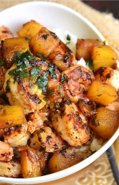 a white bowl filled with chicken and potatoes next to a fork on top of a yellow plate