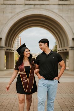 a young man and woman in graduation gowns are walking through an archway with their arms around each other