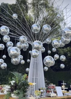 a table topped with lots of shiny silver balls next to a tall metal tree sculpture