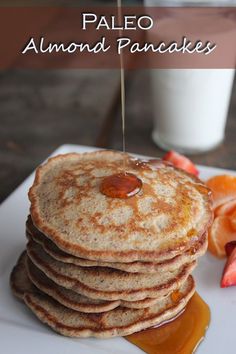 pancakes with syrup being drizzled over them and sliced fruit on the side