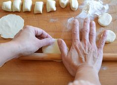 a person is rolling out dough on a wooden table with other food items around them