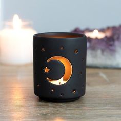 a black candle holder sitting on top of a wooden table next to a lit candle