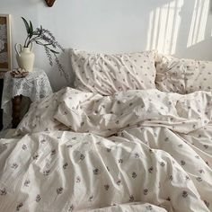 an unmade bed with white sheets and flowers on the comforter next to a shelf