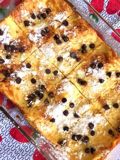 a casserole dish with chocolate chips and powdered sugar on top, sitting on a patterned table cloth