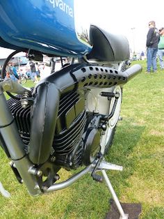 a motorcycle parked on top of a lush green field next to other people in the background