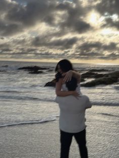 a woman carrying a man on her back while walking along the beach at sunset or sunrise