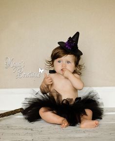 a baby wearing a witch costume sitting on the floor with her hands in her mouth