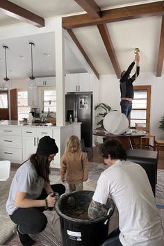 a group of people standing around a black trash can in a living room next to a kitchen