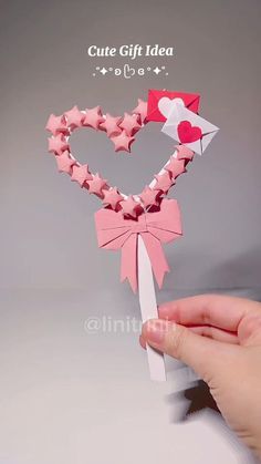 someone is holding up a heart shaped origami decoration with pink bows and hearts