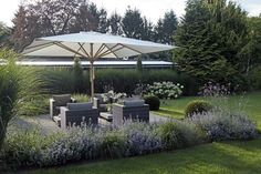 an umbrella is in the middle of a garden with couches and flowers around it