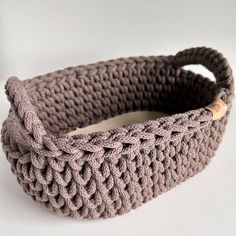 a crocheted basket is sitting on a white surface and has a wooden handle