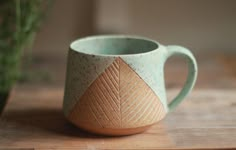 a coffee cup sitting on top of a wooden table next to a potted plant