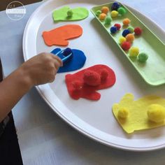 a child's hand is holding a paper plate with colorful felt fish shapes on it