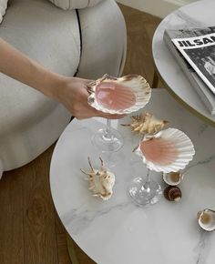 a person is holding some seashells on a table with wine glasses and magazines