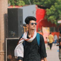 a young man walking down the street with his scarf around his neck and sunglasses on