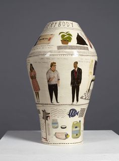 a vase with pictures of people on it sitting on a white table next to a gray wall