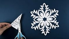 someone cutting out a paper snowflake on a blue wall with scissors and glue