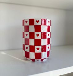 a red and white checkered coffee cup with hearts on the inside is sitting on a shelf