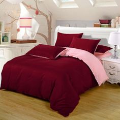 a bed with red sheets and pillows in a room next to a white dresser under a slanted ceiling