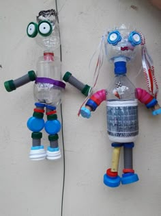 two plastic robots hanging from the side of a wall next to each other on strings