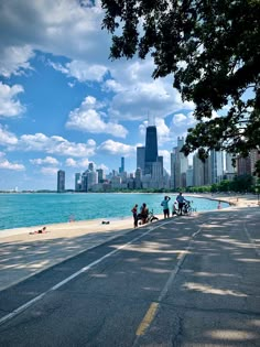 people standing on the side of a road next to water with buildings in the background