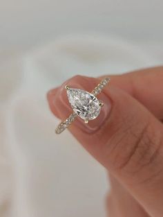 a woman's hand holding an engagement ring with a pear shaped diamond