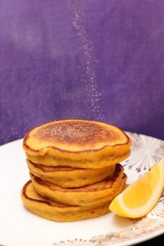 a stack of pancakes sitting on top of a white plate next to a slice of lemon