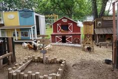 several chickens and roosters are in a small yard with many different colored buildings around them