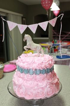 a birthday cake with pink frosting and a white horse figurine on top