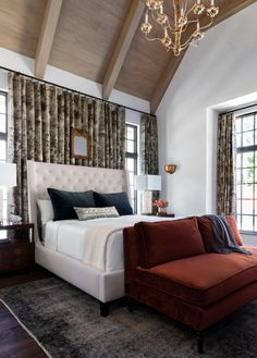 a large bed sitting under a chandelier in a bedroom next to two windows