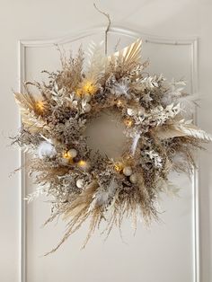 a wreath hanging on the front door decorated with white and gold ornaments, lights and feathers