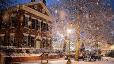 a snowy night in front of an old brick building with trees and benches on the sidewalk