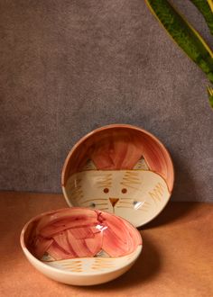 two bowls with designs on them sitting next to a potted plant