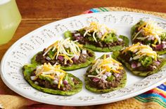 some tacos are sitting on a white plate next to a glass of green juice